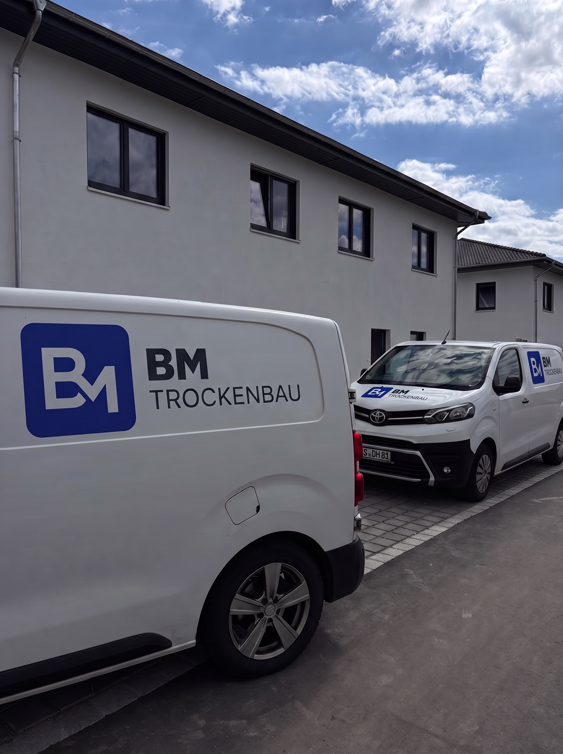 Zwei BM Trockenbau Firmenfahrzeuge vor einem Neubau